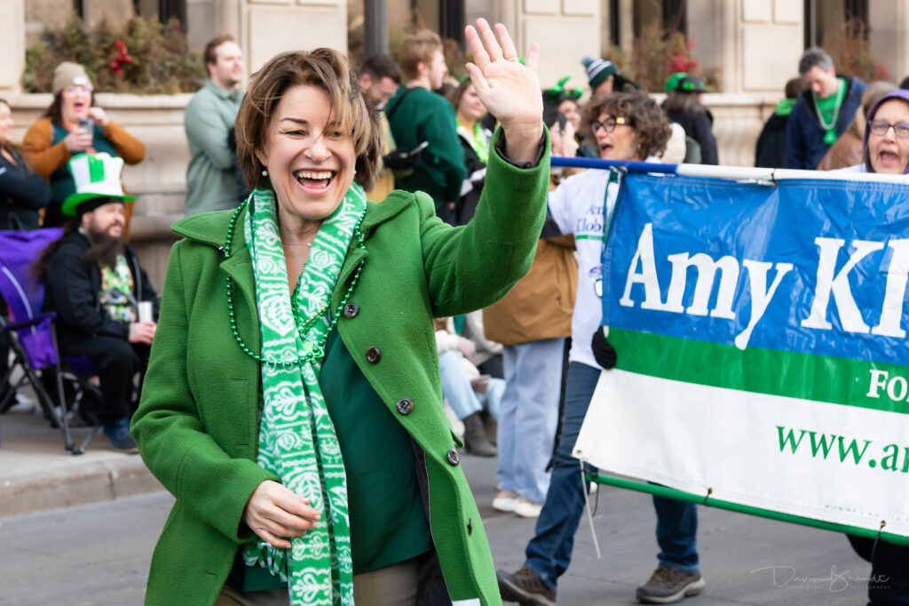 Senator Amy Klobuchar waving while walking in a parade. 