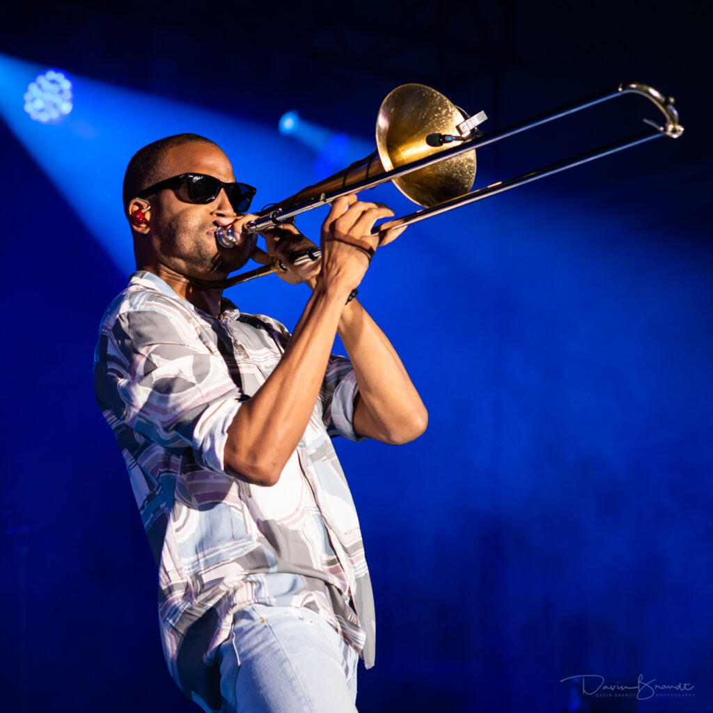 Trombone Shorty blowing with blue background